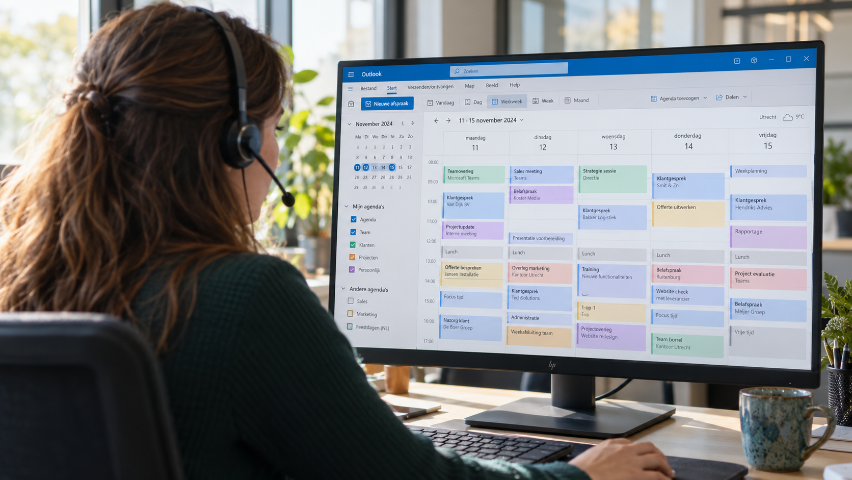 Medewerker met headset van achteren gezien bij een computerscherm met een volle Outlook-agenda.